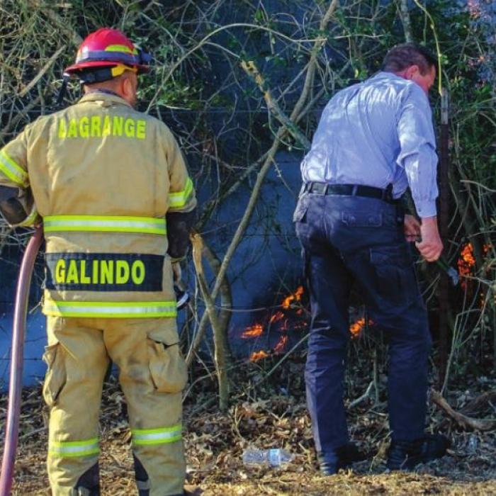 Above, La Grange Fire Chief Frank Menefee cuts down a barbed wire fence while firefighter Antonio Galindo gets ready to attack the blaze with a water hose. Below, firefighters put out a burning tree that they cut down. Photos by Andy Behlen