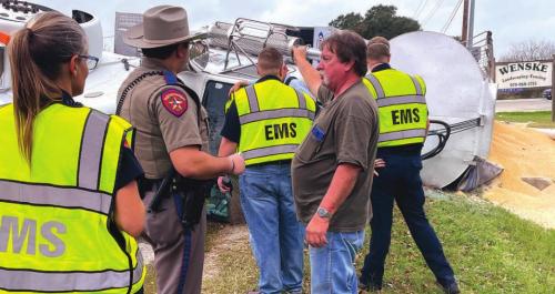 18-wheeler driver Jirrel Dean Warren of Seguin speaks with DPS Trooper Josh Berger Friday after a wreck, as county EMS officials respond to the scene. Warren took evasive action to avoid a wreck with another vehicle, but spilled his corn load. He was taken to St. Mark’s for evaluation. Photo by Andy Behlen