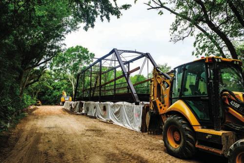 The Willow Springs Bridge currently sits on the south bank of Cummins Creek while contractors build new concrete approaches. Pct. 2 Commissioner Luke Sternadel said it took a 100-ton crane to pick up and move the bridge. The bridge itself does not weigh that much, but it took such a large piece of machinery due to the tricky nature of navigating the creek-bottom terrain.