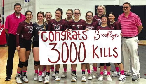 With her teammates and coaches joining her, Fayetteville’s Brooklyn Jaeger (seventh from left) holds up a banner congratulating her on reaching the milestone of 3,000 career kills after Friday’s match versus Mumford. Photo courtesy of Lisa Dyer