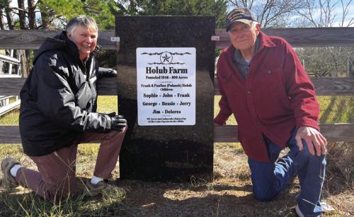 Delores Schmitt, left, and her brother Jim Holub, pose next to the sign that Jim put up honoring their parents’ farm on what remains of their family land on Holub Lane after 90% of it was claimed by LCRA and the City of Austin when building the power plant 50 years ago. Photo by Jeff Wick