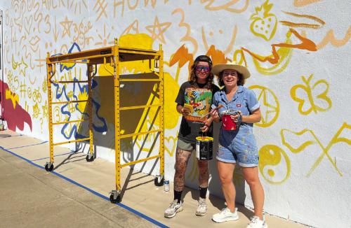 Artists Avery Houser, right, and Sullivan Meservey, left, in the early stages of their mural work on Main Street Monday. The artists’ process of “doodle grid” is shown. Those words and smaller pictures will not be part of the final design but are actually just a fun way to grid out their design on a larger surface without using either a ruler or a projector. Photo by Jeff Wick