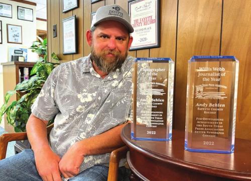 Andy Behlen sits next to two prestigious awards he won at this year’s 96th annual South Texas Press Association awards – Journalist of the Year and Photographer of the Year.