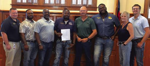 Pictured are representatives of the Real Deal Family Reunion and County and State officials with the mass gathering permit approved by County Judge Dan Mueller last Friday: (from left) Fayette County EMS Director Josh Vandever, Cody Wilson, Roderick Devaughn, Real Deal President Ronald Addison, Sgt. Ron Naumann of the Fayette County Sheriff’s Office, Nathaniel Patterson, Fayette County Emergency Management Coordinator Angela Hahn, and Donald Jirasek of the Texas Dept. of Health and Human Services.