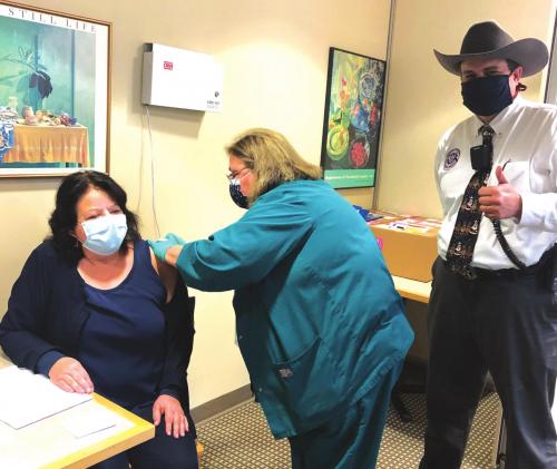 Laurie Quitta, left, Nurse Director of the Medical Surgical Unit of St. Marks Medical Center, gets injected with the COVID vaccine by nurse Dabbie Hinkley, center, as Craig Moreau, Emergency Management Chief, gives a thumbs up.