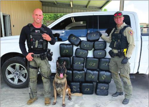 Left to right: Sgt. Randy Thumann, canine offi cer Kolt and Deputy David Smith stand next to their lates find, 182 pounds of marijuana.