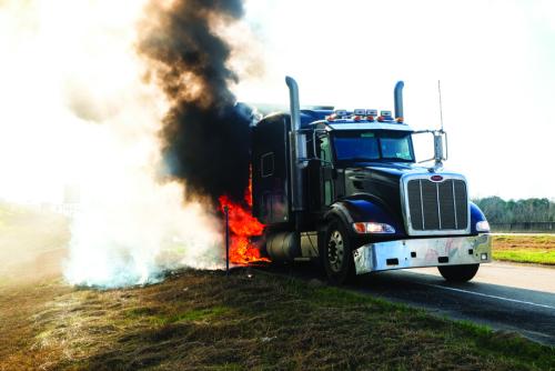 Above, a Peterbilt truck pulling a piece of oilfield equipment caught fire after a tire blow out on SH 71 at the Whataburger exit in La Grange Wednesday morning. Below, La Grange Fire Chief Frank Menefee sprays down the smoking rear axle where the fire started. Photos by Andy Behlen