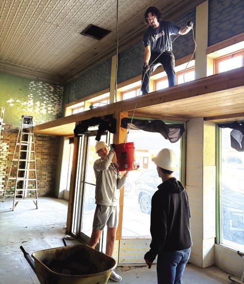 Garrett Reavis, up top, lowers down a bucket of old brick paneling to Deacon Wick and Jude Lira Saturday. All are Fayette Community Theatre volunteers who showed up Saturday to help with initial demolition work at the old Prause’s Meat Market, which will be a new theatre. Photos by Chrystal Wick