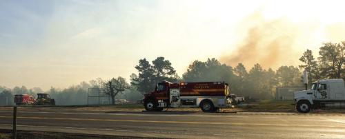 A La Grange fire tanker staged along US 77 near Camp Lost Pines as a plume of smoke from the Whirling Pines Fire rises in the air behind it. Photo by Andy Behlen