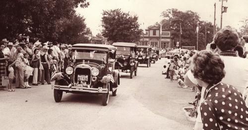 Parade spectators are lined up around the parade route people can be seen waving U.S flags. A group of antique cars are in the parade line up and the Apothecary is visible in the background. Circa 1970s. Photos courtesy of Rox Ann Johnson of the Fayette Heritage Museum and Archives