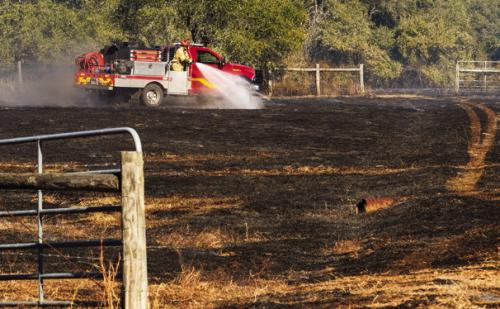 A La Grange fire truck sprays water on smouldering hot spots at a grass fire north of La Grange Friday. Photo by Andy Behlen