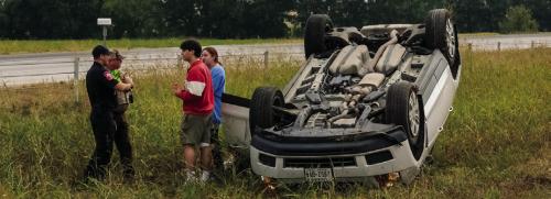 First responders speak to the driver and passenger of a Cadillac SUV that rolled over on SH 71 near Plum on Thursday. No one was seriously injured. Photo by Andy Behlen