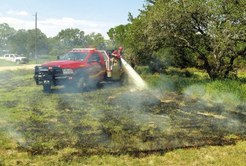 La Grange firefighter Colton Whitaker sprays down a patch of burning grass on Chaparral Rd. last Wednesday. Photo by Andy Behlen